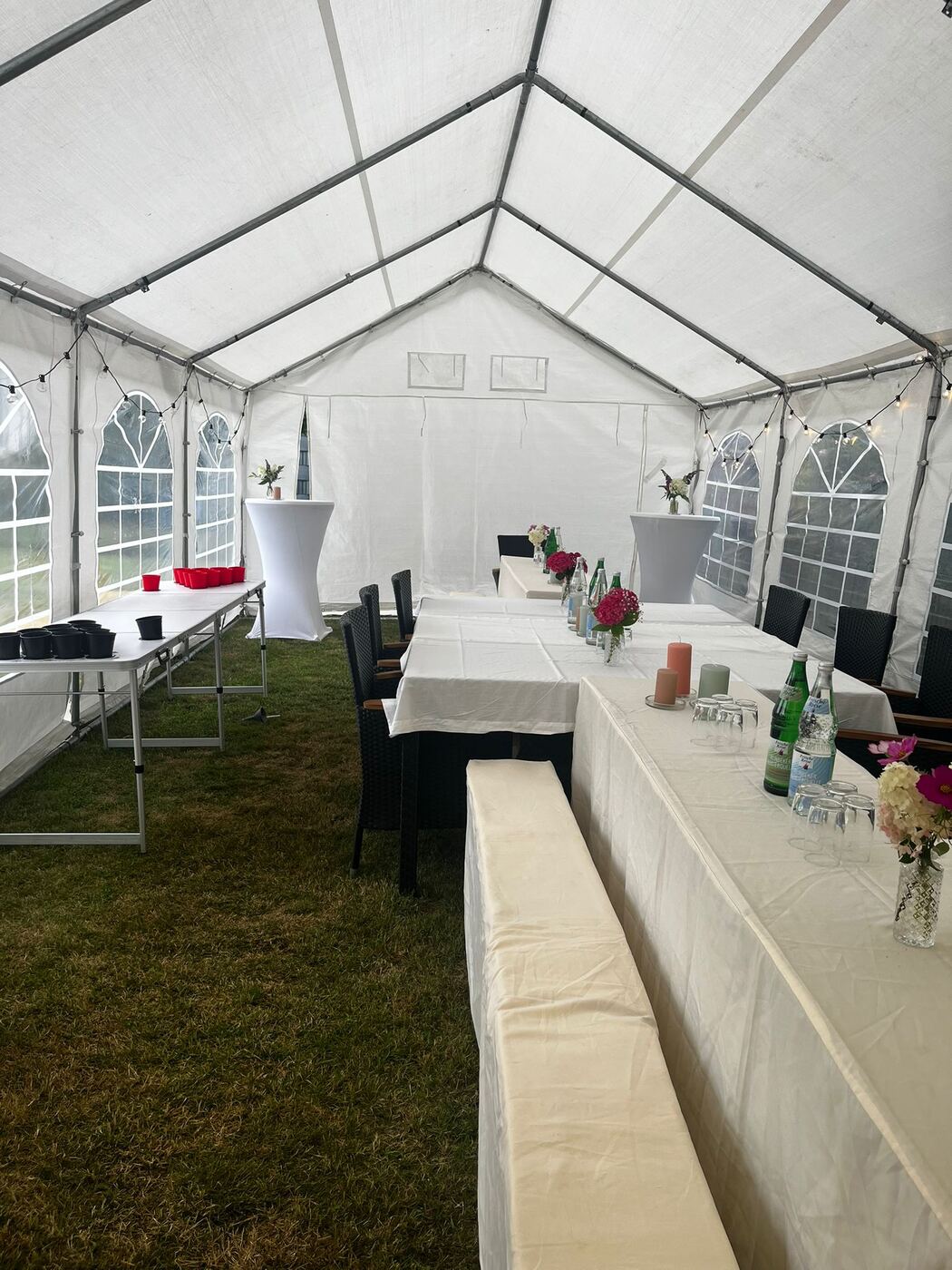 Liebevoll eingedeckte Tische im Zelt mit Blumen und Kerzen